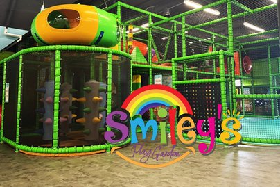 buntes Logo von Smileys Play Garden im Hintergrund das grüner Klettergerüst